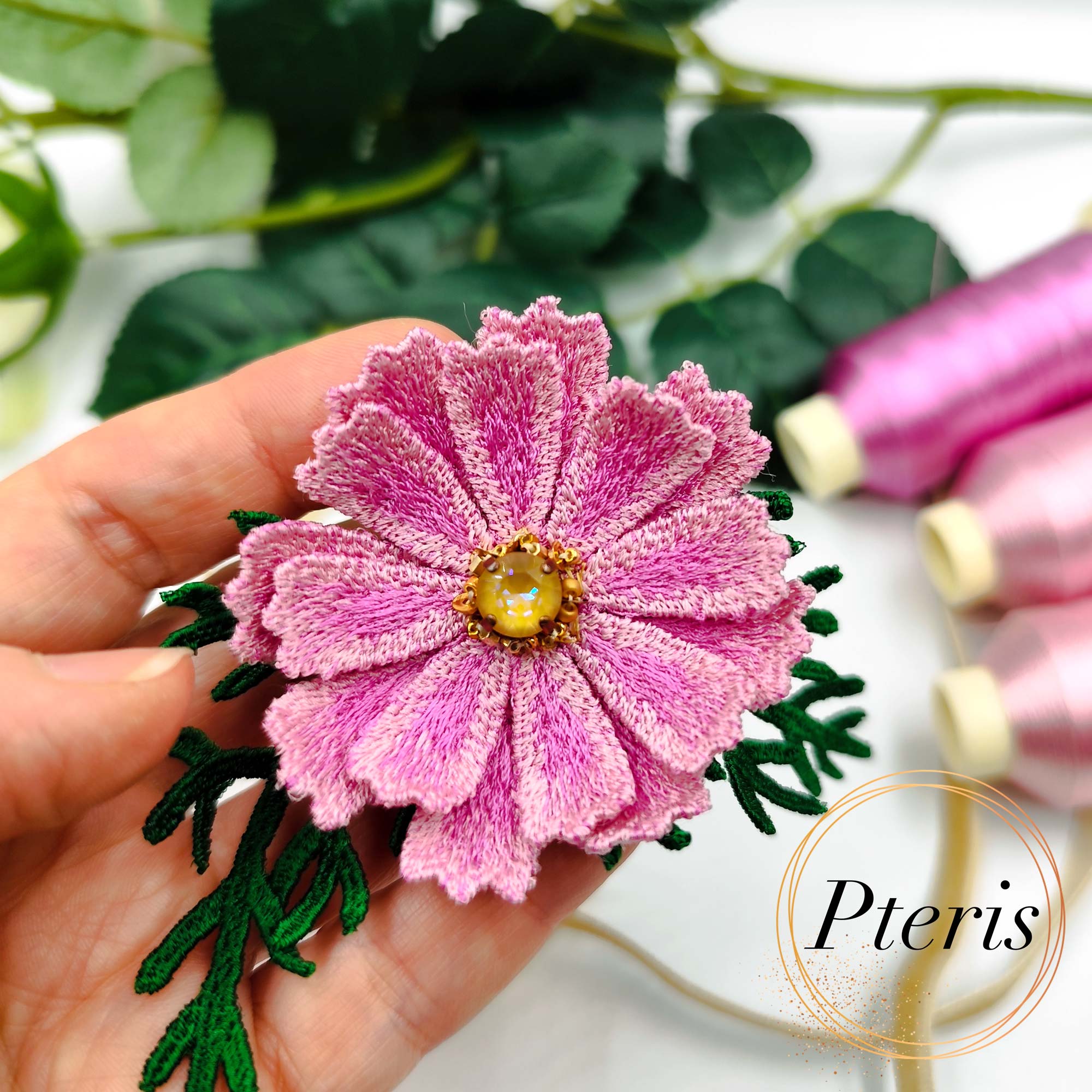 3D Cosmos Embroidery Design for FSL brooch featuring layered pink petals with a golden center and dark green feathery leaves.