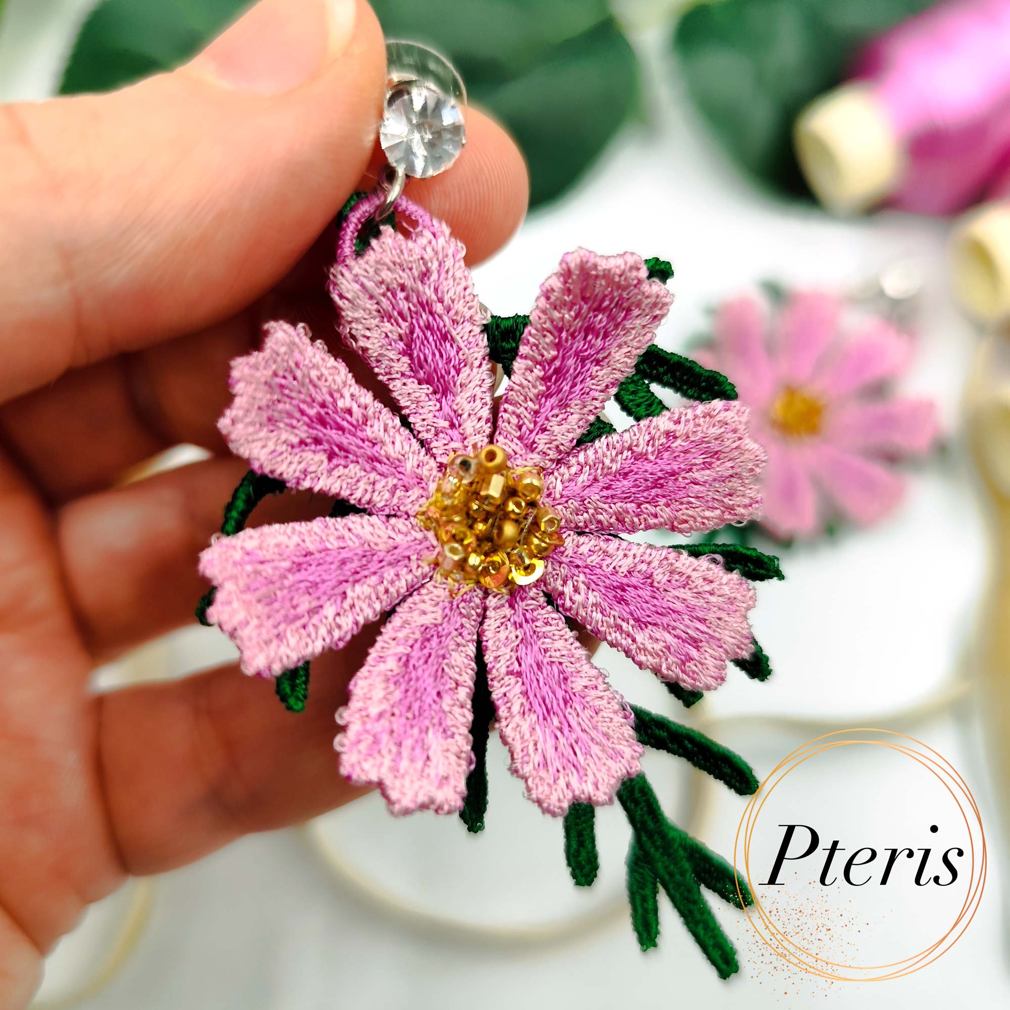 3D Cosmos Embroidery Design for FSL jewelry featuring bright pink petals, golden beaded centers, and green textured leaves on crystal stud earrings.