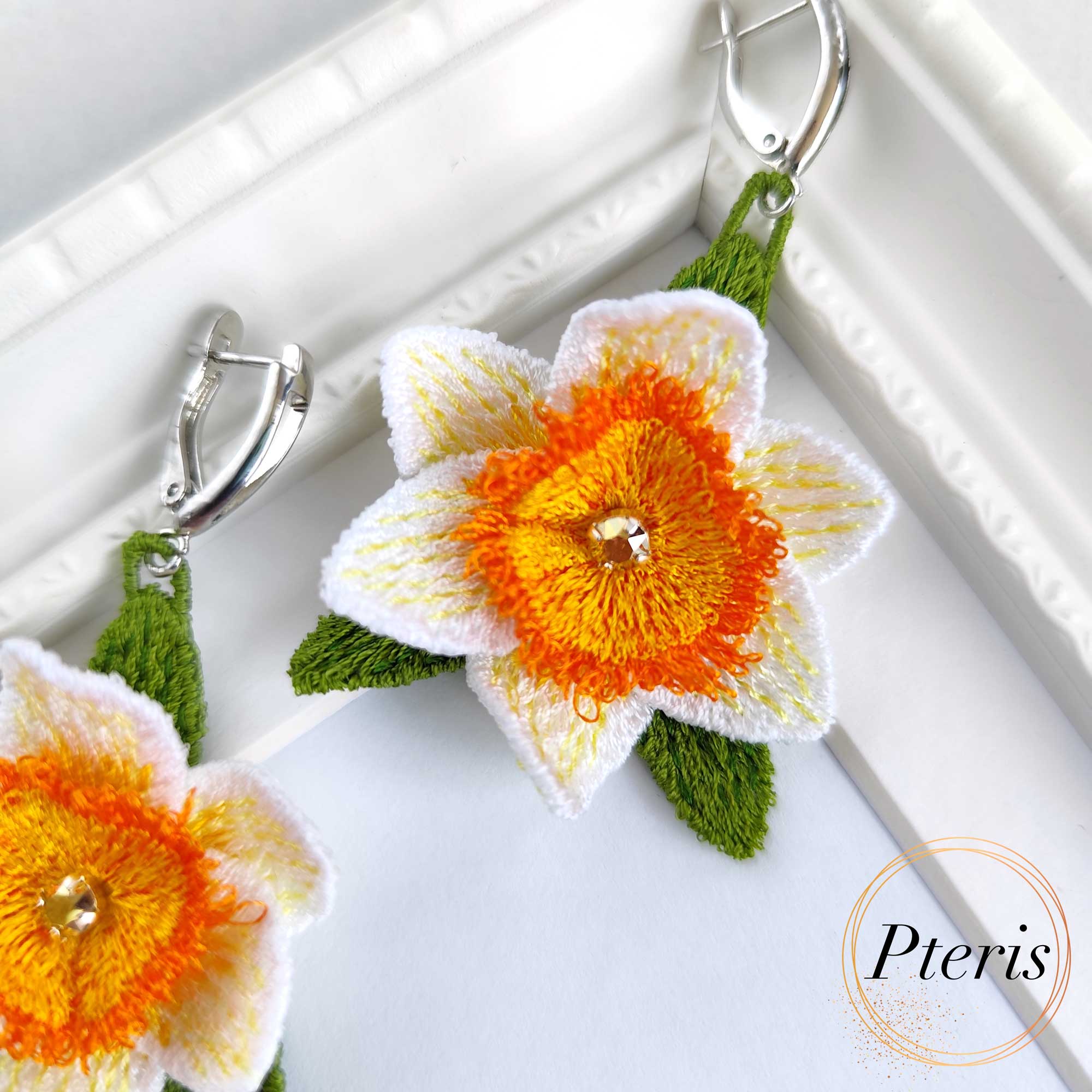FSL 3D Daffodil earrings machine embroidery design with white and orange petals and green leaves on silver hooks.
