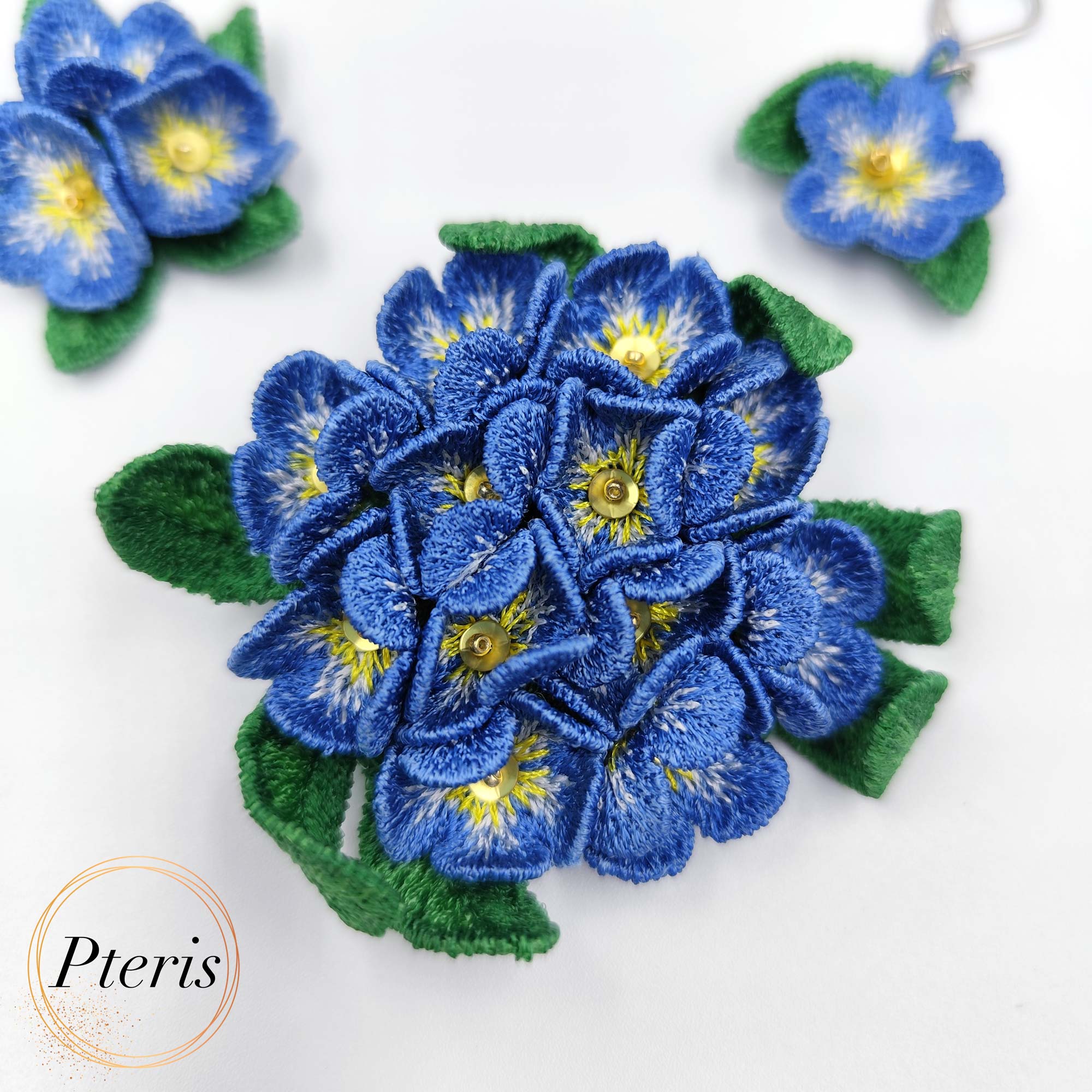 3D Forget-Me-Not Embroidery Design for FSL jewelry featuring blue flowers with yellow centers and green leaves on silver hooks.
