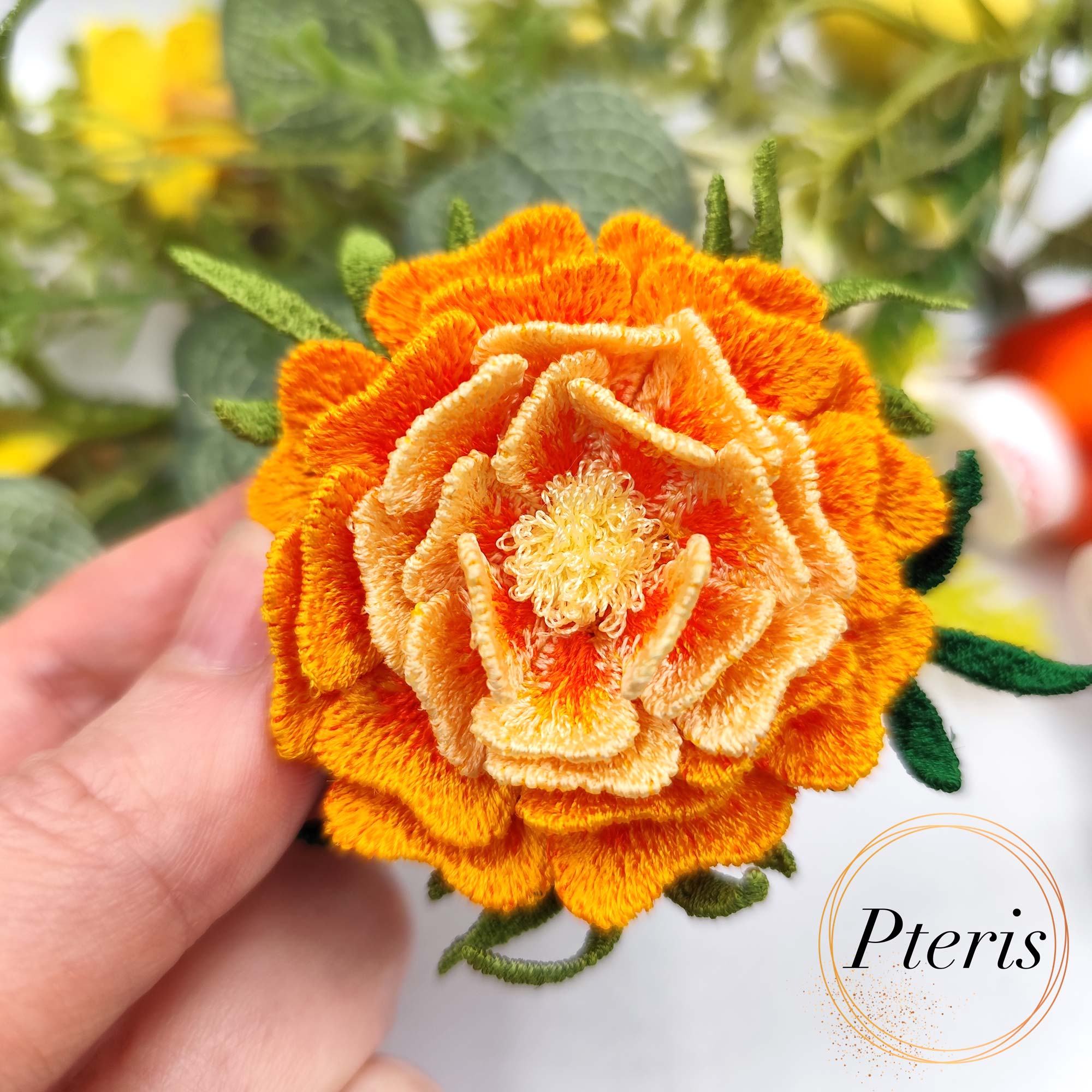 3D Marigold Embroidery Design for FSL brooch featuring layered orange and yellow ruffled petals with dark green leaves.