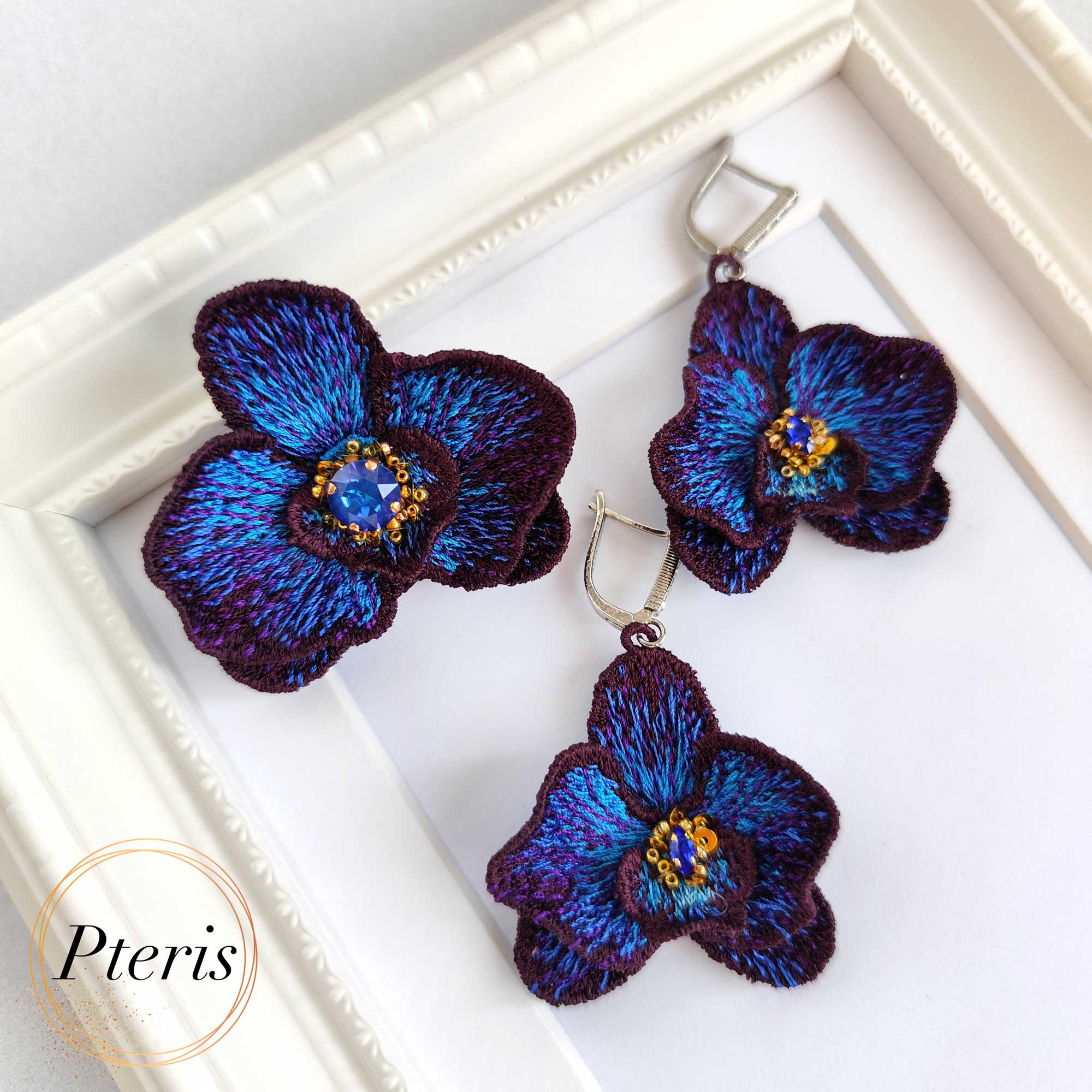 FSL 3D Orchid earrings and brooch machine embroidery design featuring dark purple and bright blue gradient petals with a central crystal accent.