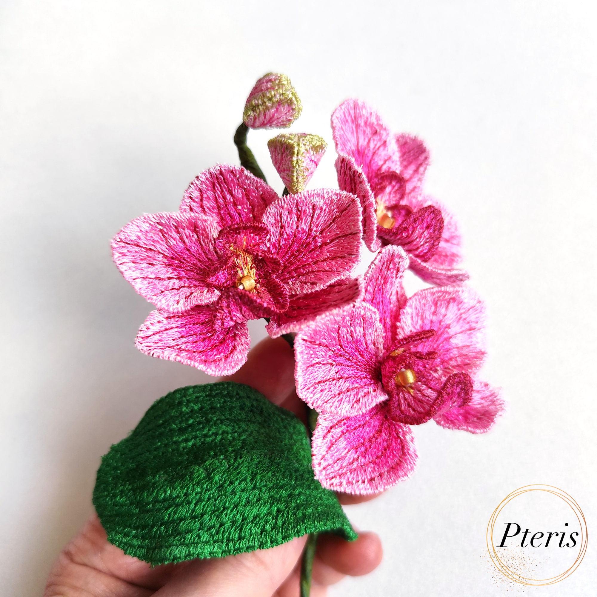 3D Phalaenopsis Orchid Embroidery Design featuring pink textured flowers, delicate green buds, and a broad green leaf on a branch.