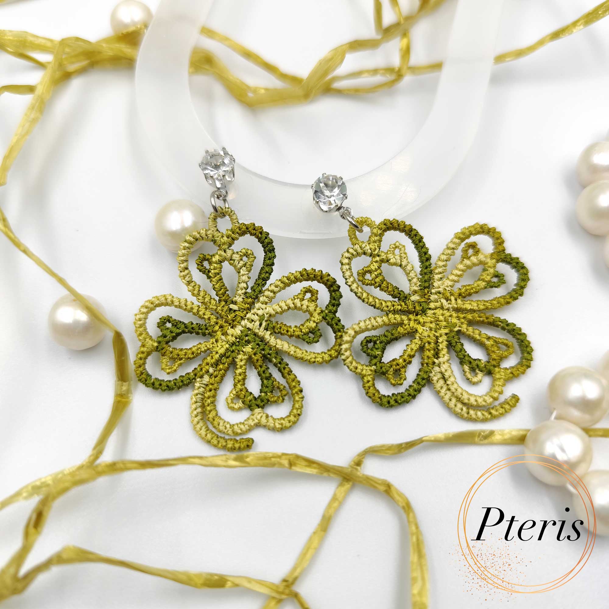 FSL Clover Earrings Embroidery Design featuring a pair of green tatting-style lace clover earrings with crystal studs, displayed among pearls and gold ribbons.