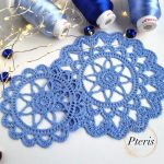 FSL Crochet Coaster Embroidery Design featuring two blue freestanding lace doilies with an intricate floral-web pattern, styled with blue thread spools and fairy lights.