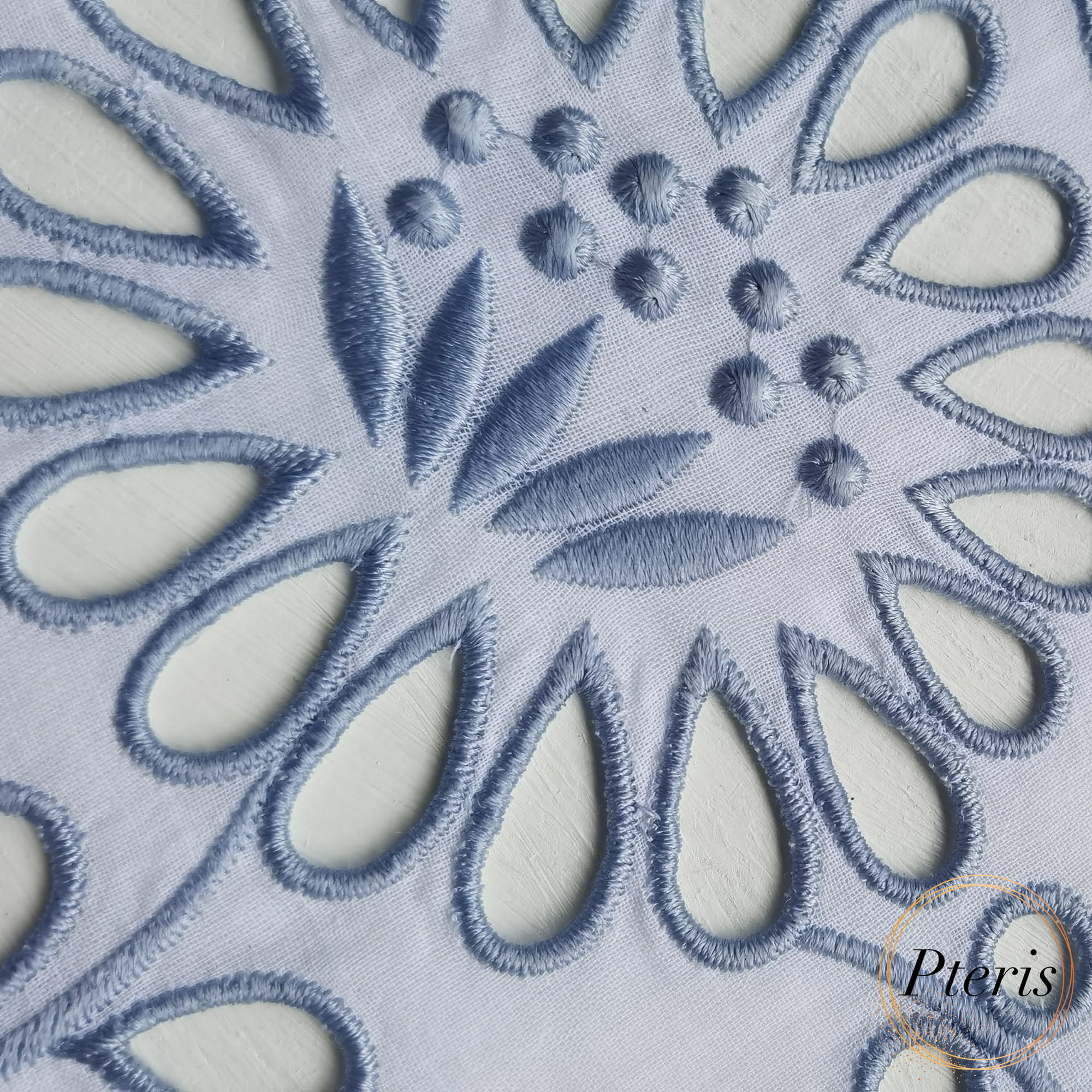 Machine embroidery Richelieu technique showcasing blue thread satin stitches around fabric cutouts and textured embroidered dots.