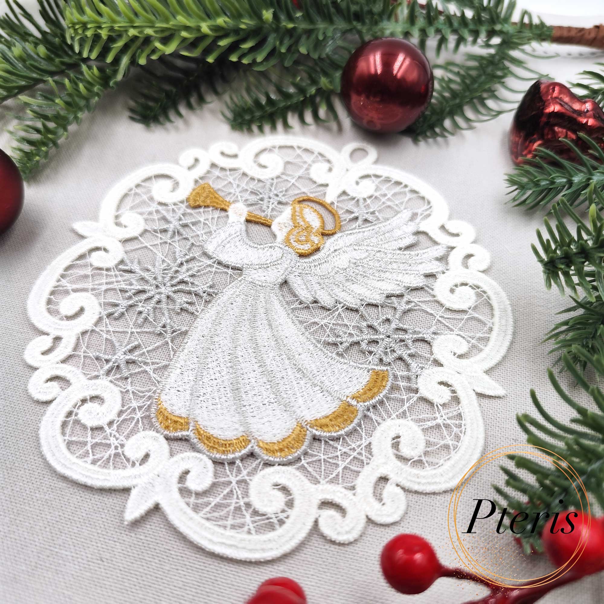 FSL Trumpeting Angel Suncatcher embroidery design featuring two white and gold freestanding lace medallions with angels, styled on a grey background with pine branches and red Christmas ornaments.