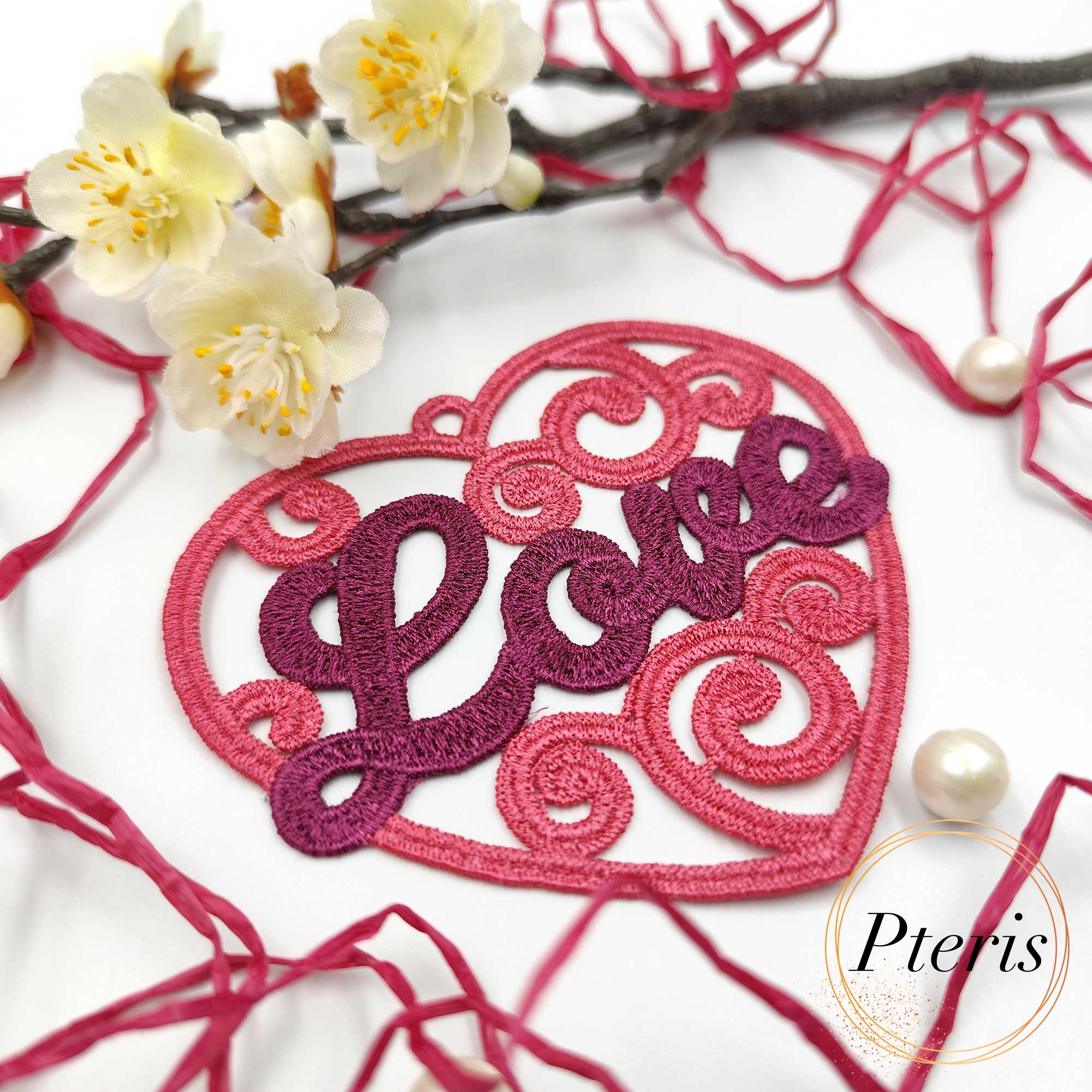FSL Love Heart Suncatcher embroidery design featuring a pink and purple freestanding lace heart with "Love" script, styled with white spring blossoms and pearls.