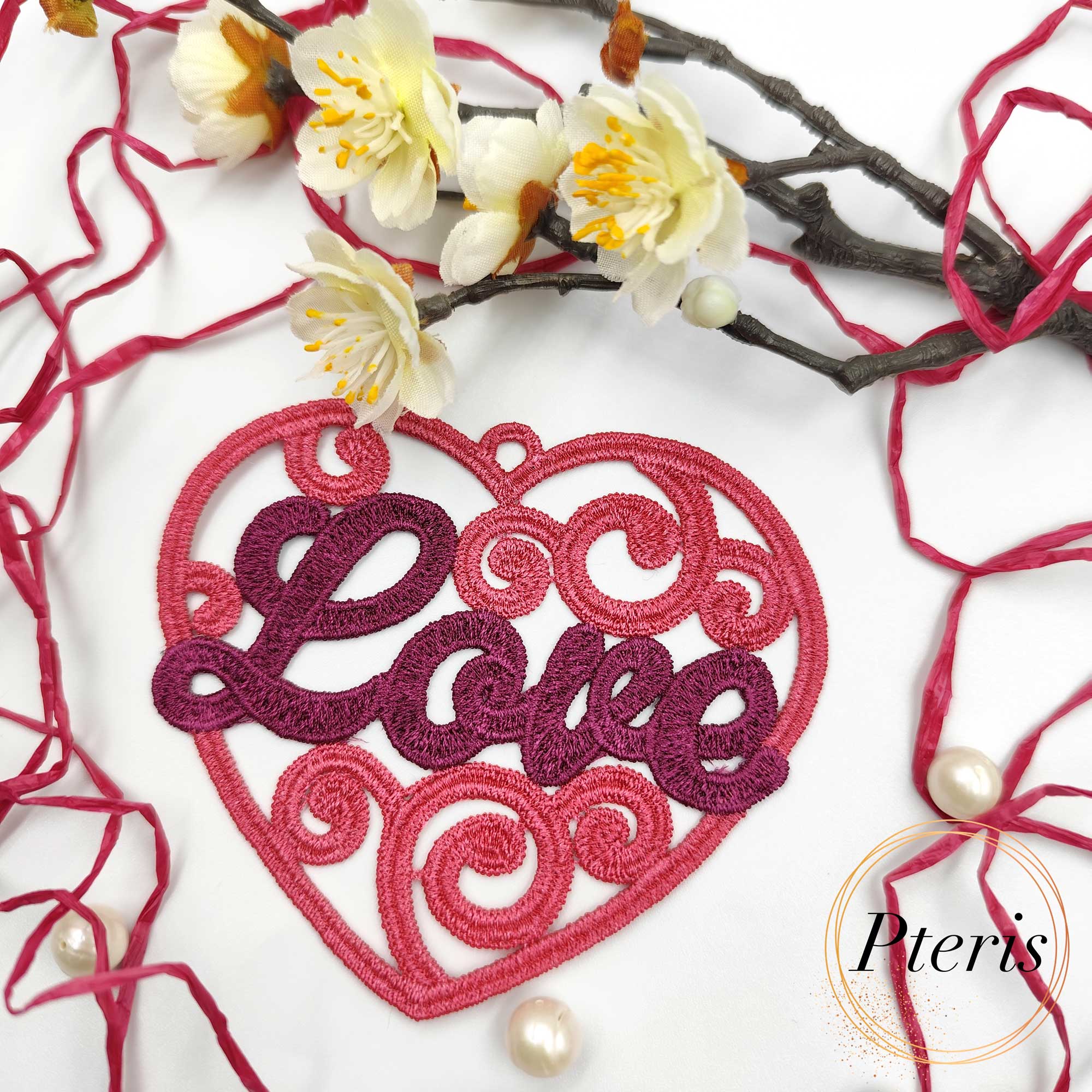 FSL Love Heart Suncatcher embroidery design featuring a pink and purple freestanding lace heart with "Love" script, styled with white spring blossoms and pearls.