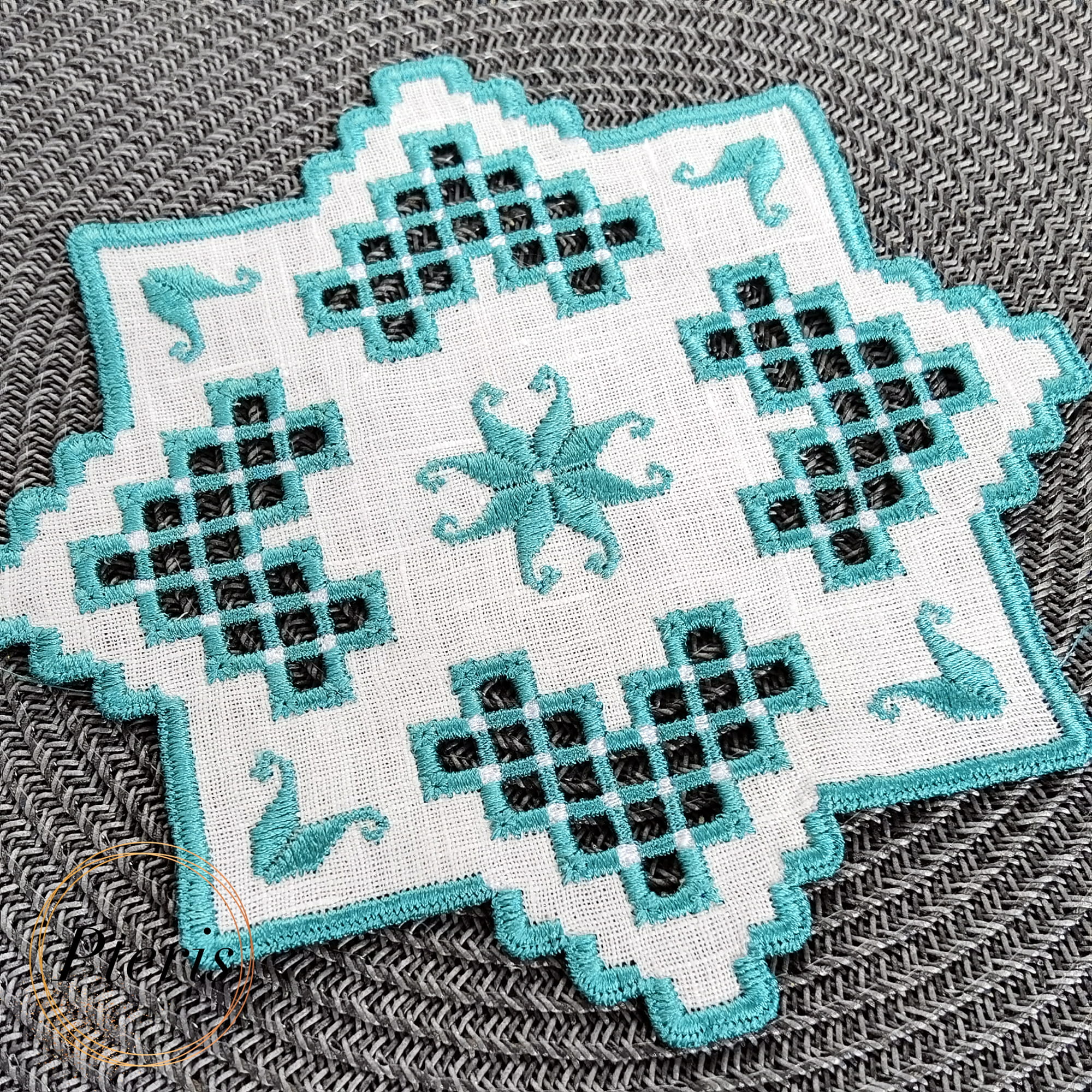 Blue Hardanger machine embroidery design featuring a white square cocktail napkin with intricate blue lace cutwork and star motifs, styled with silver ornaments and pine branches.