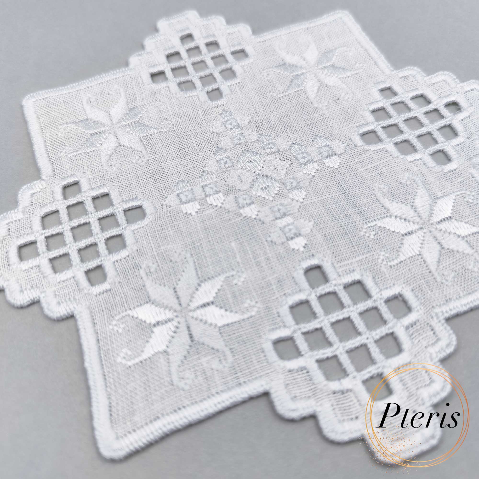 Hardanger machine embroidery design featuring a white square cocktail napkin with intricate lace cutouts and star motifs, styled on a grey background with pine branches and a star-shaped ornament.