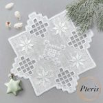 Hardanger machine embroidery design featuring a white square cocktail napkin with intricate lace cutouts and star motifs, styled on a grey background with pine branches and a star-shaped ornament.
