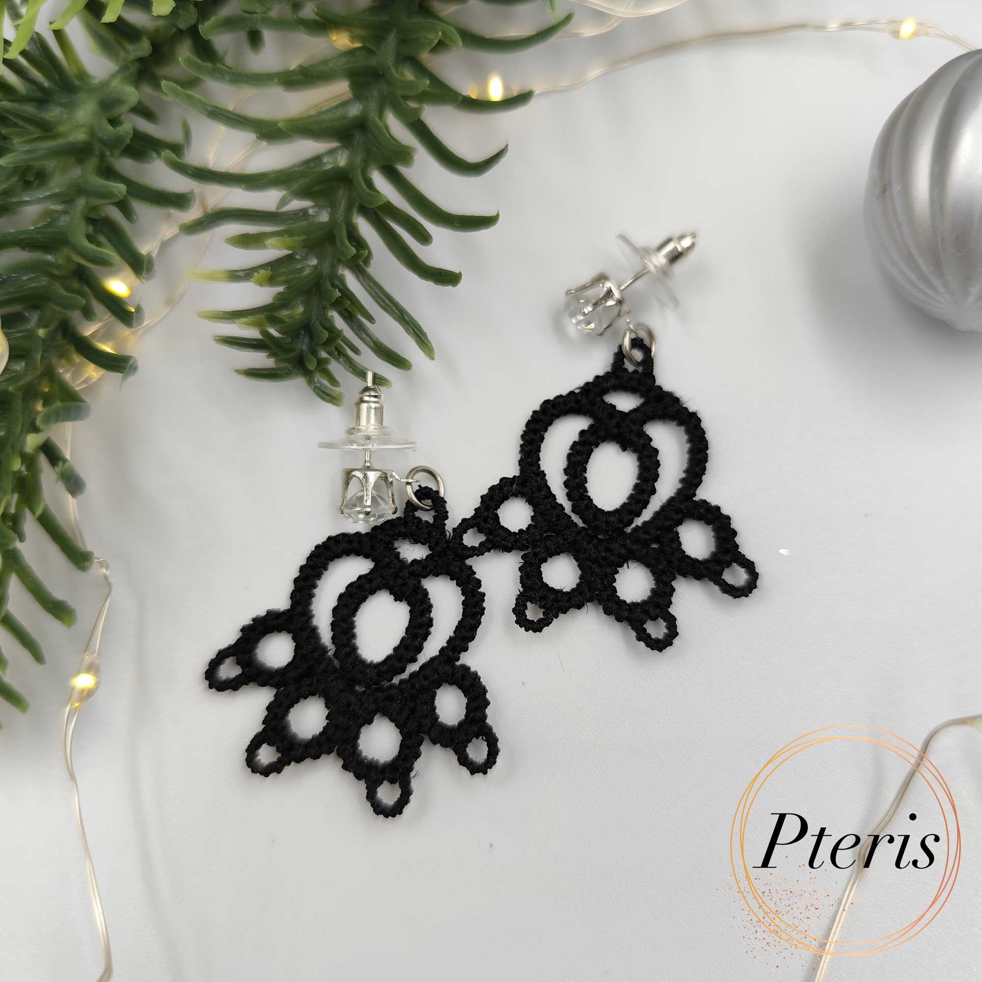 FSL Cat Paw Earrings Embroidery Design showing a pair of black tatting-style lace earrings shaped like cat paws on a white background with decorative leaves and berries.
