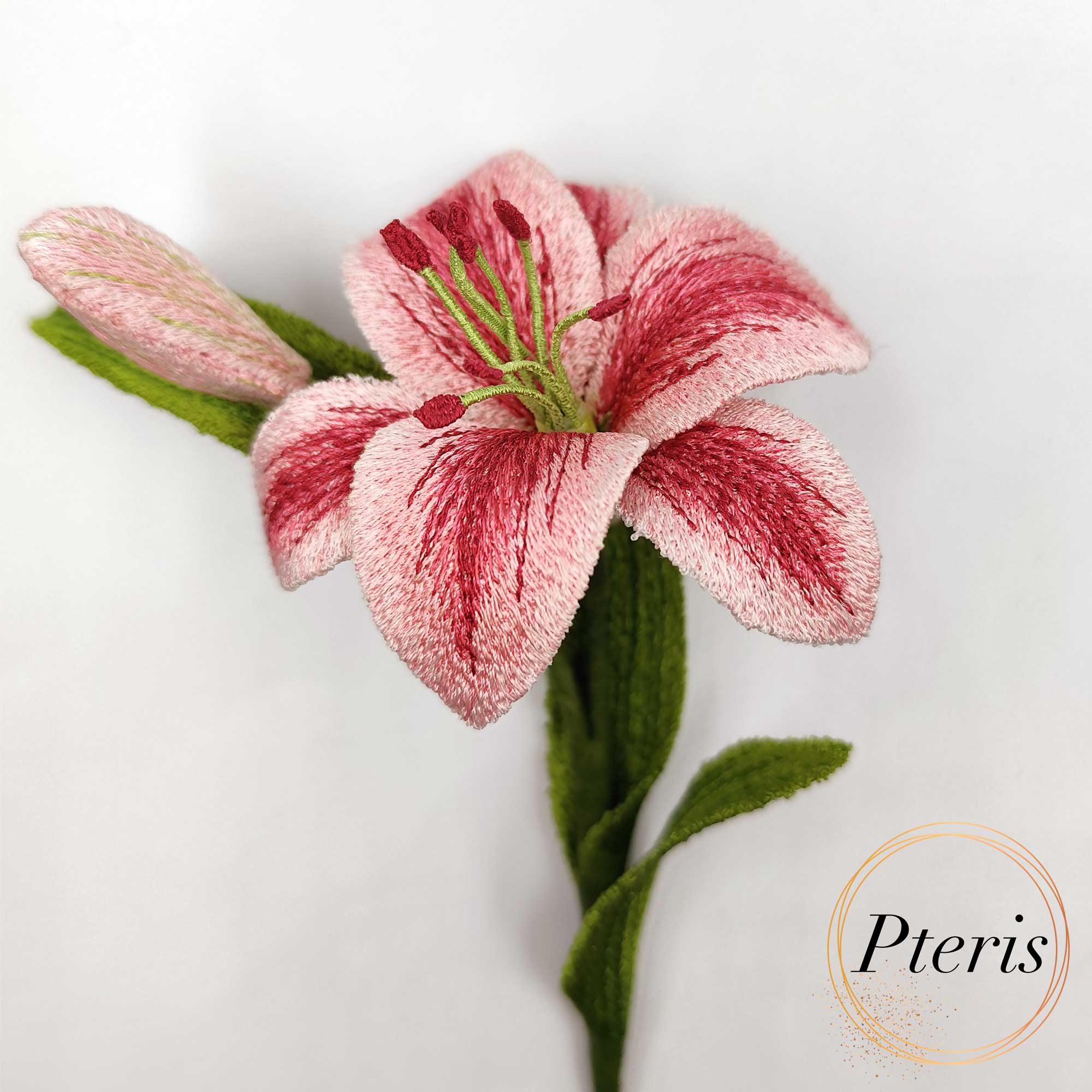 3D Lily machine embroidery design featuring a hand holding a highly detailed freestanding pink and red embroidered lily flower with a realistic green stem, bud, and textured leaves.