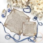 ITH Lace Cocktail Napkin embroidery design showing two different sized linen napkins with beige lace borders, styled with white flowers, blue beads, and miniature blue and white clogs.