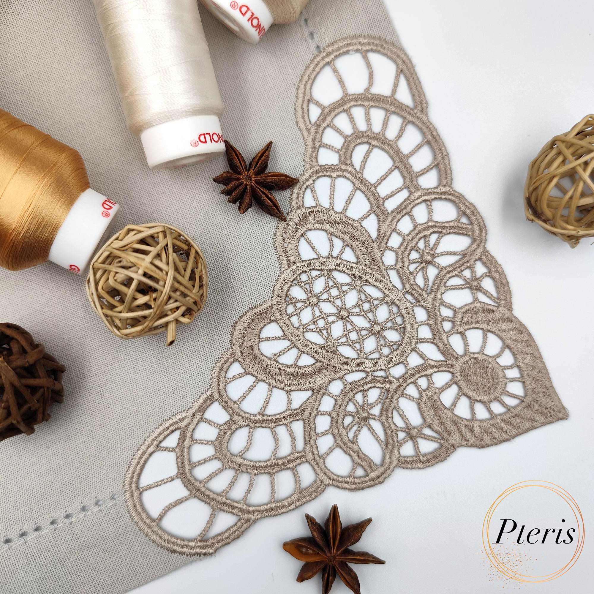 FSL Lace Napkin Corner embroidery design featuring an intricate champagne-colored lace border stitched onto a linen napkin, styled with white spring blossoms and a thread spool.