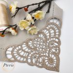 FSL Lace Napkin Corner embroidery design featuring an intricate champagne-colored lace border stitched onto a linen napkin, styled with white spring blossoms and a thread spool.