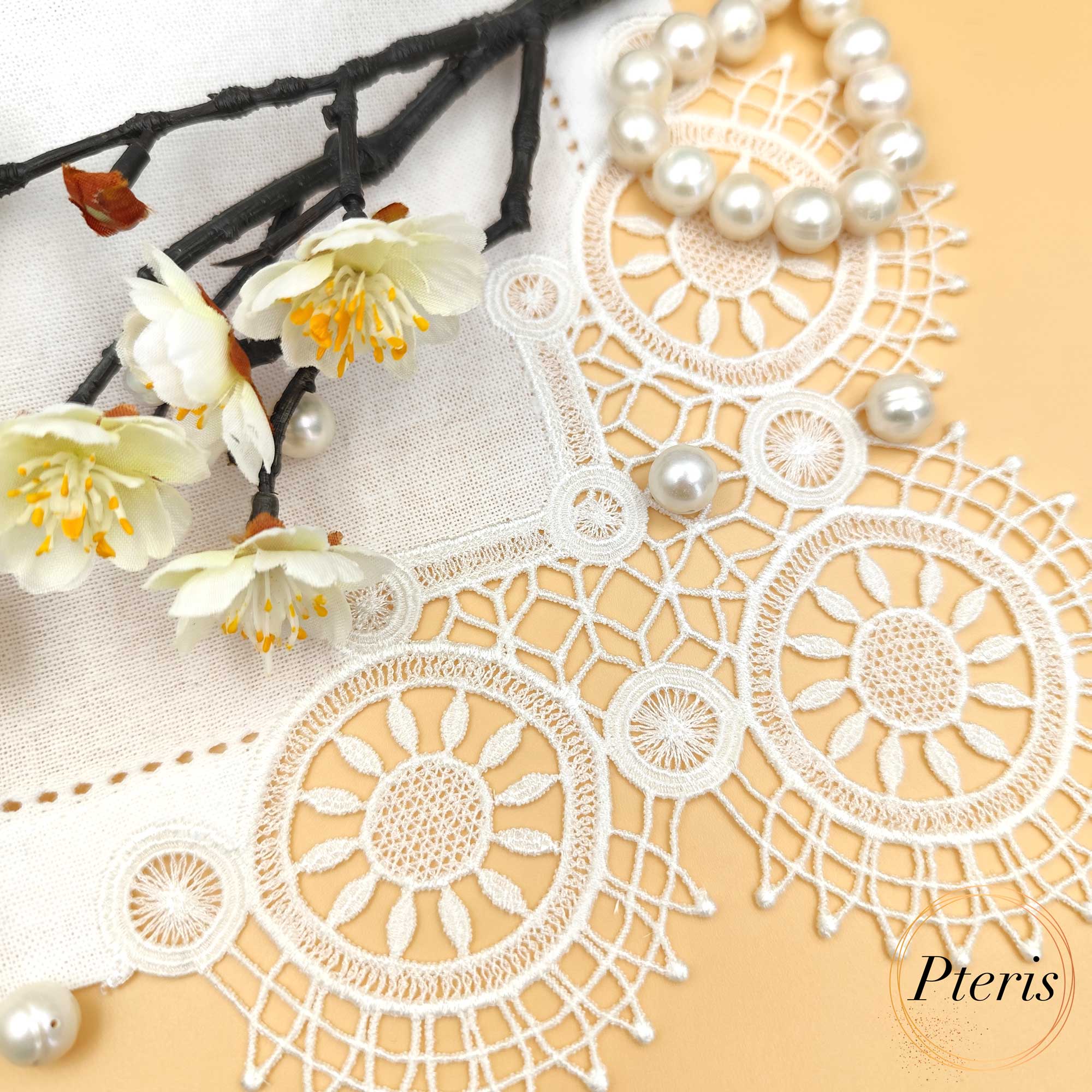 FSL Lace Napkin Corner embroidery design featuring white freestanding lace circular motifs stitched onto a linen napkin, styled with pearls and white blossoms on a peach background.