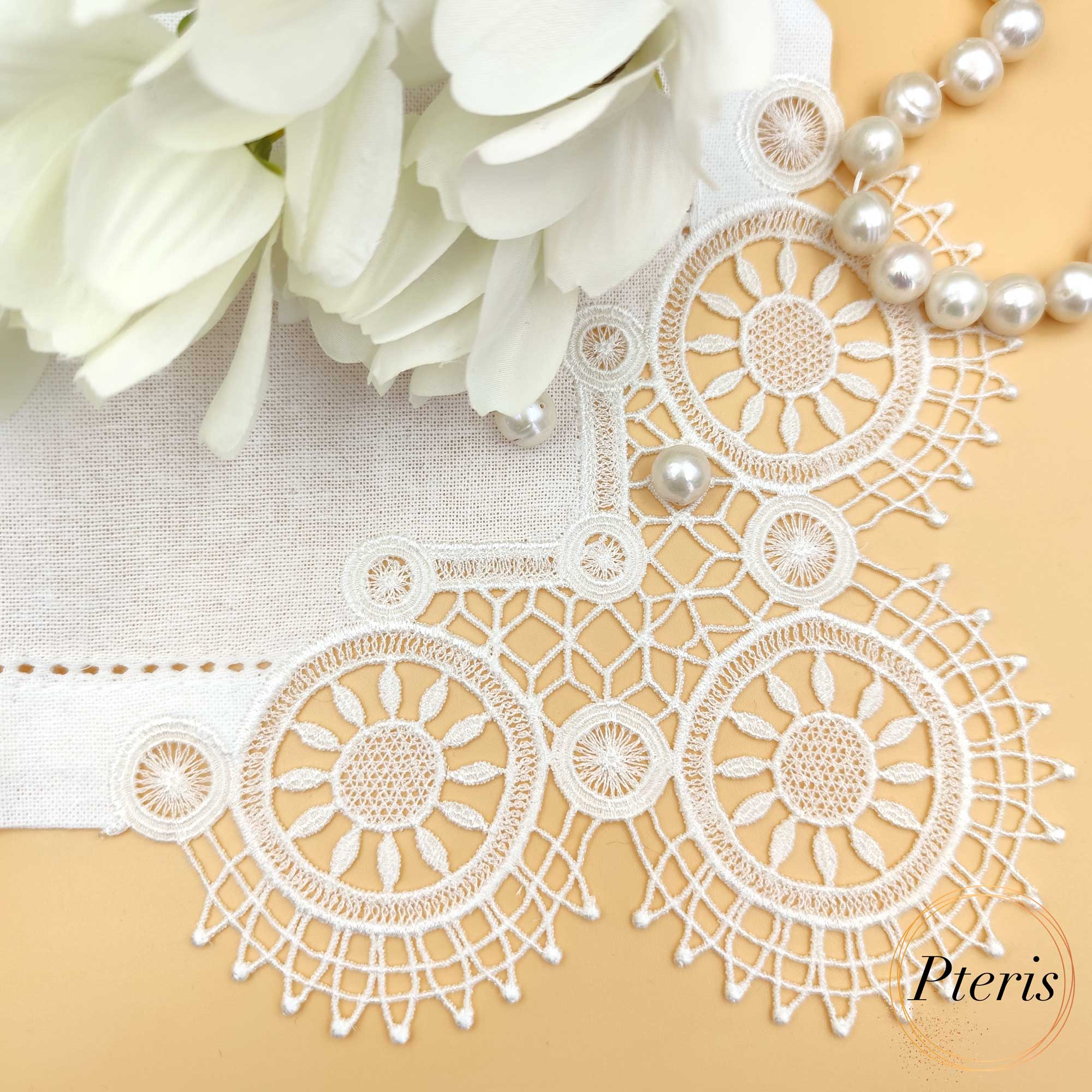 FSL Lace Napkin Corner embroidery design featuring white freestanding lace circular motifs stitched onto a linen napkin, styled with pearls and white blossoms on a peach background.