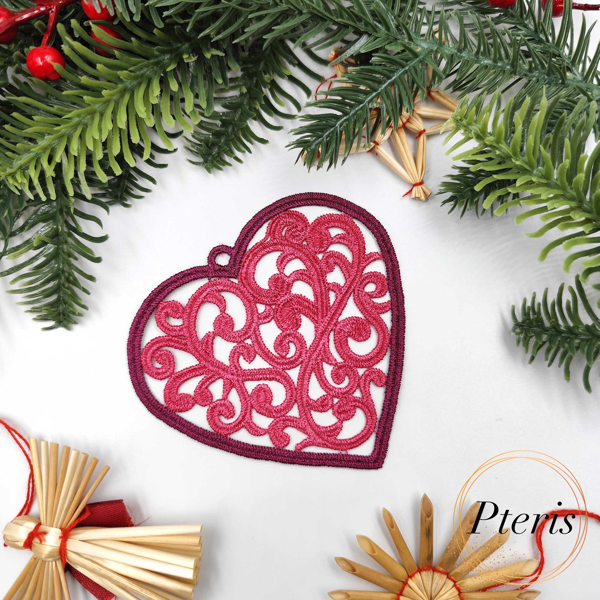 FSL Filigree Heart Suncatcher embroidery design featuring a pink freestanding lace heart with intricate scrolls, styled on a white background with pine branches and Christmas ornaments.