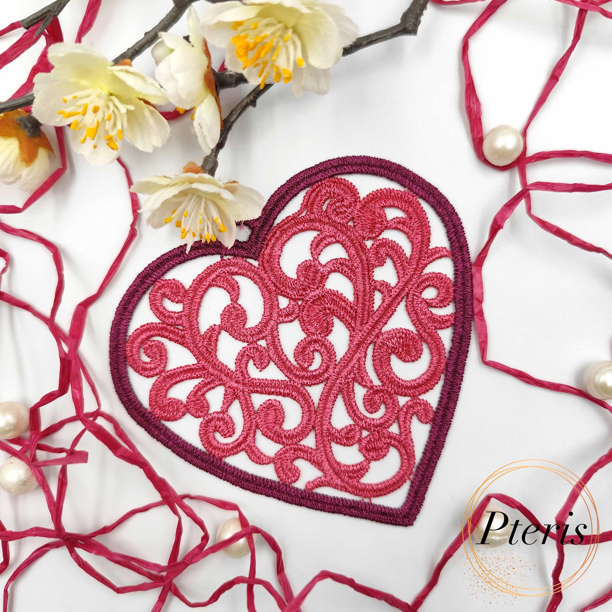 FSL Filigree Heart Suncatcher embroidery design featuring a pink freestanding lace heart with intricate scrolls, styled on a white background with pine branches and Christmas ornaments.