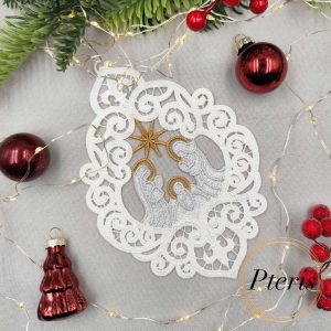 FSL Nativity Scene Suncatcher embroidery design featuring a white and gold freestanding lace ornament of the Holy Family, styled on a grey background with pine branches, red ornaments, and fairy lights.