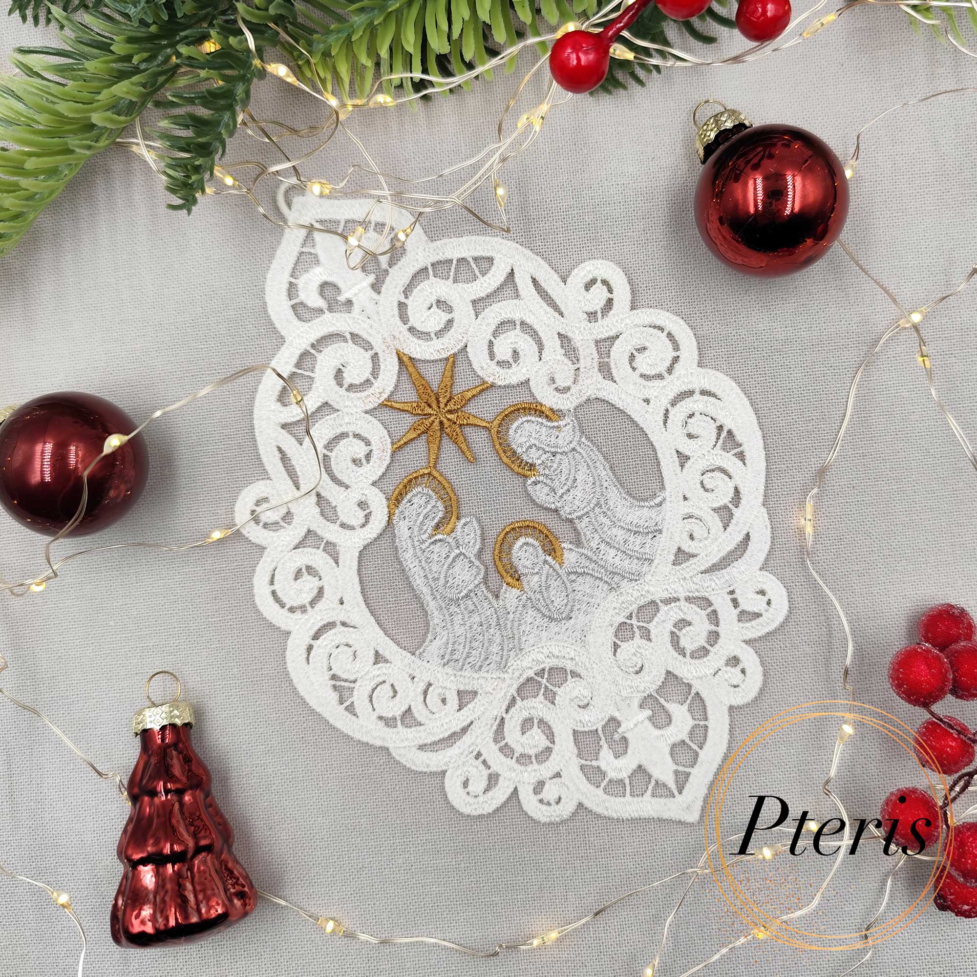 FSL Nativity Scene Suncatcher embroidery design featuring a white and gold freestanding lace ornament of the Holy Family, styled on a grey background with pine branches, red ornaments, and fairy lights.
