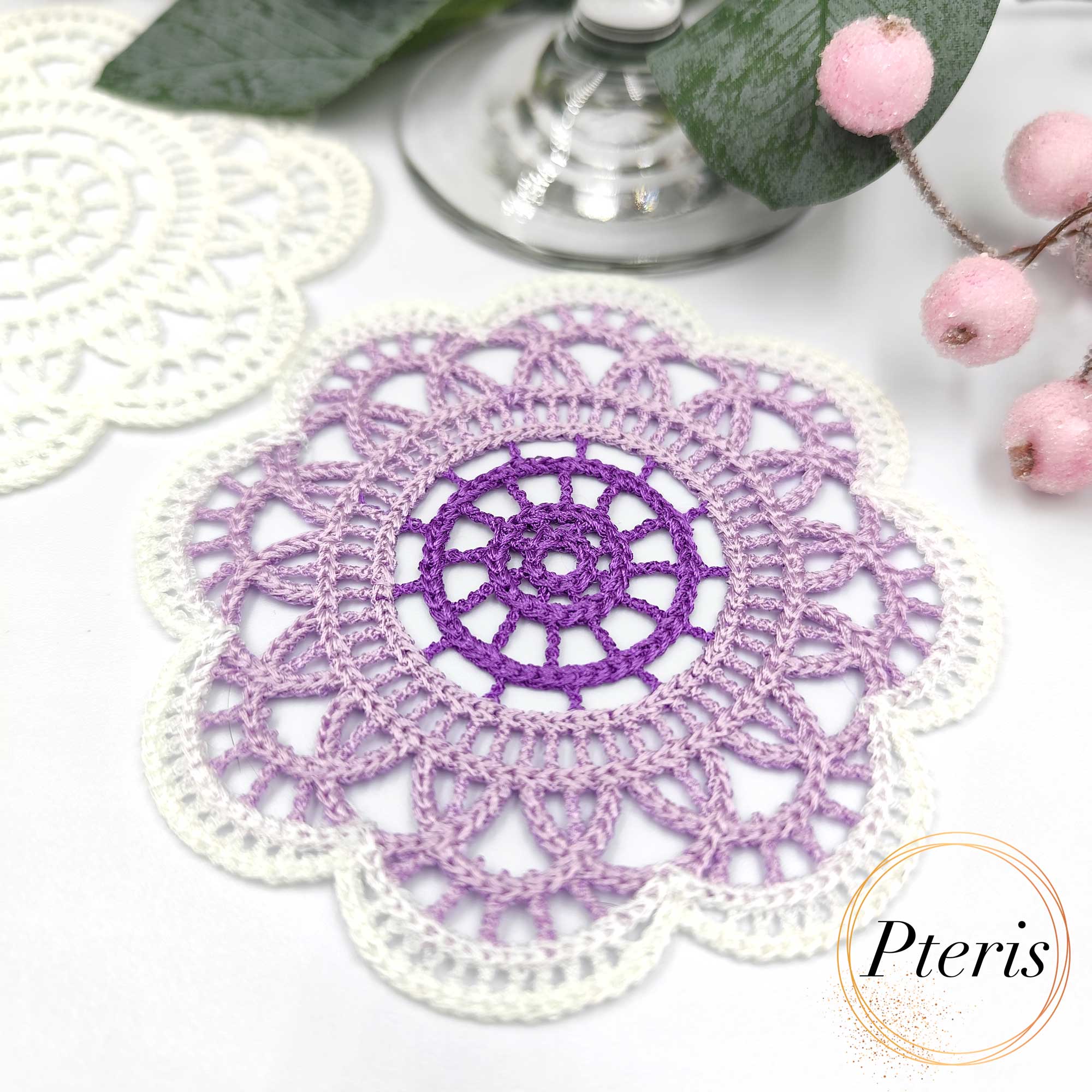 FSL Crochet Coaster Embroidery Design featuring two circular freestanding lace doilies in white and purple-gradient thread, styled with pink berries on a white background