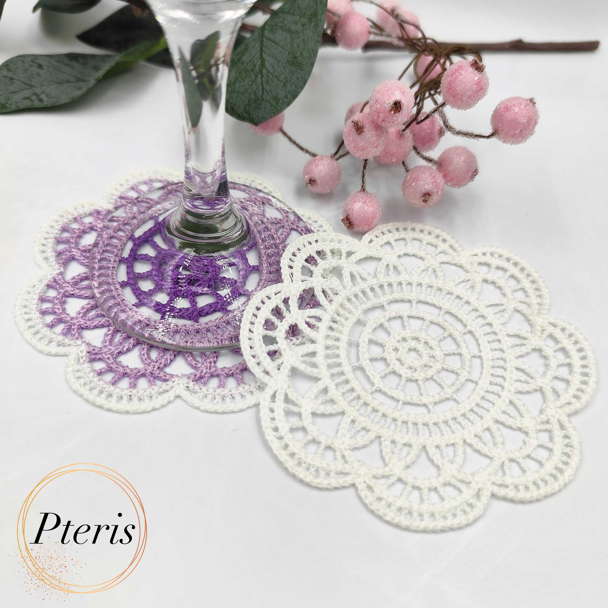 FSL Crochet Coaster Embroidery Design featuring two circular freestanding lace doilies in white and purple-gradient thread, styled with pink berries on a white background