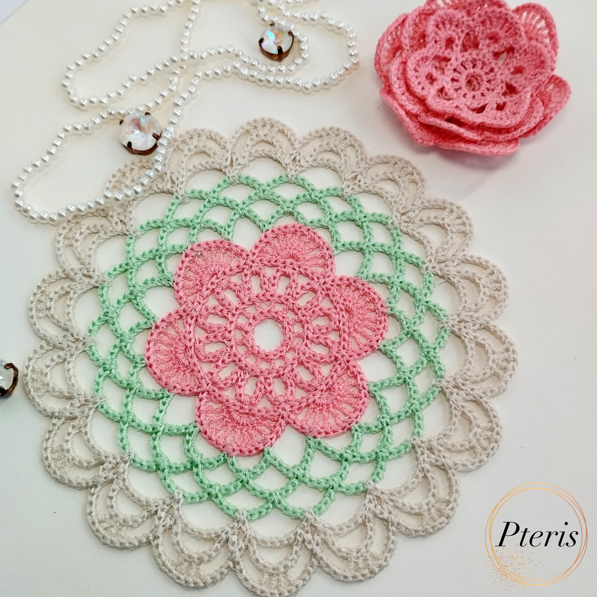 FSL 3D Rose Doily Embroidery Design featuring a pink 3D lace rose centered on a green and beige crochet-style freestanding lace doily, styled with pearls.