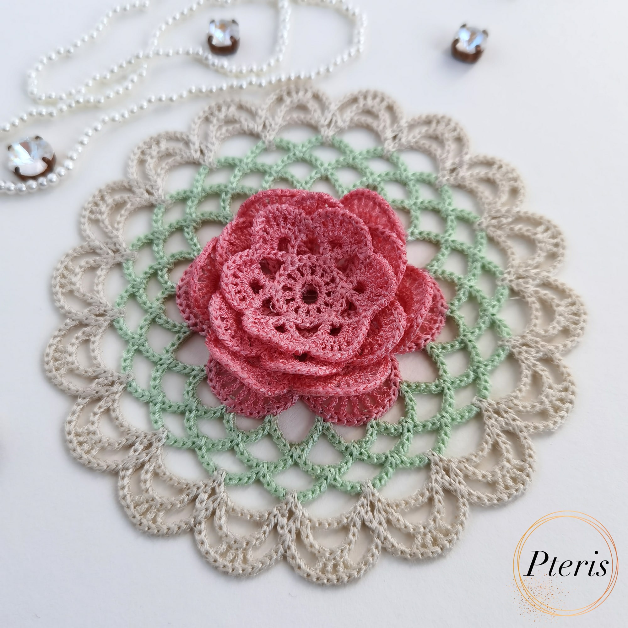 FSL 3D Rose Doily Embroidery Design featuring a pink 3D lace rose centered on a green and beige crochet-style freestanding lace doily, styled with pearls.