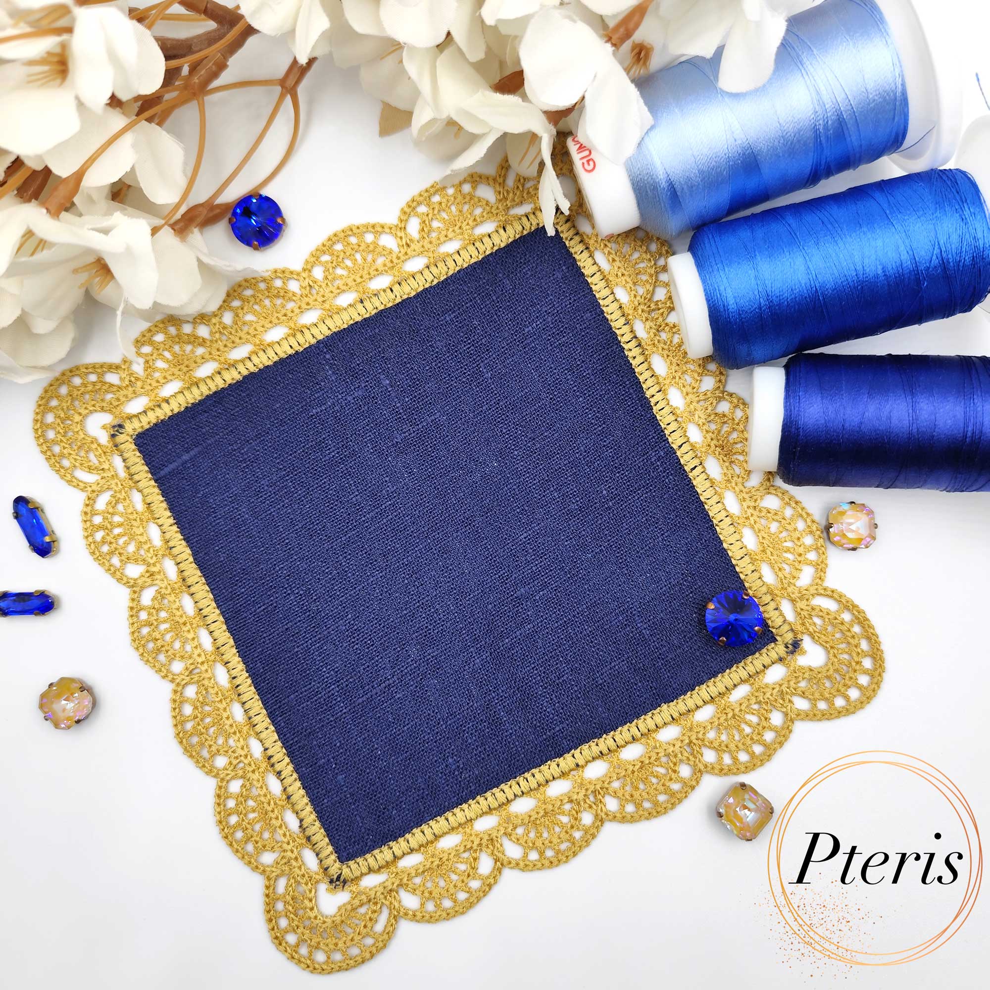 FSL Crochet Style Napkin Design featuring a square navy blue linen center surrounded by an intricate gold freestanding lace border, displayed with blue embroidery threads.