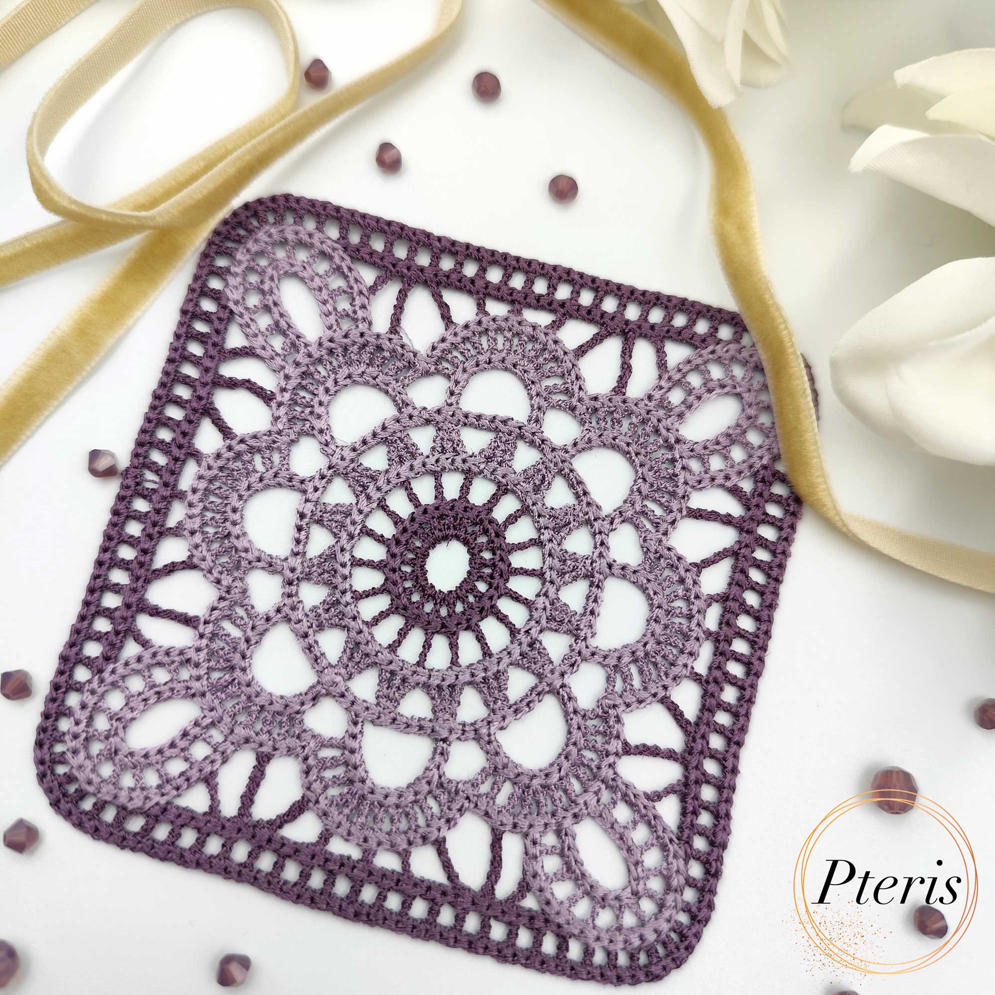 FSL Granny Square Crochet Design featuring two square freestanding lace coasters in shades of purple gradient, styled with white flowers and a gold ribbon.