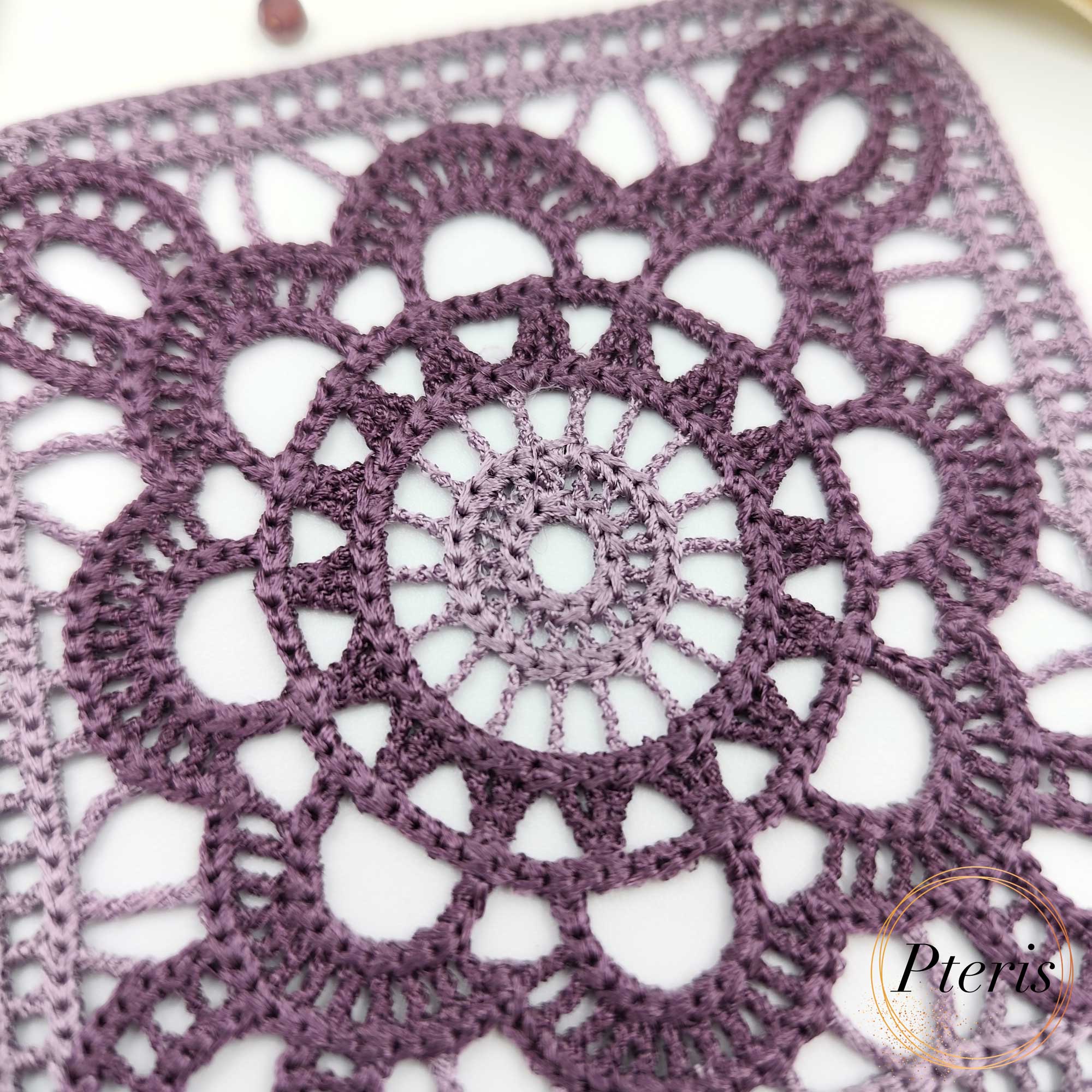 FSL Granny Square Crochet Design featuring two square freestanding lace coasters in shades of purple gradient, styled with white flowers and a gold ribbon.