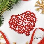 FSL Tatting Heart Pendant Design featuring a bright red freestanding lace heart ornament suspended by a ribbon, surrounded by festive evergreen branches and straw stars.