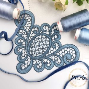 FSL Lace Napkin Corner embroidery design featuring intricate dusty blue freestanding lace stitched onto a white linen napkin, styled with matching blue thread spools and velvet ribbon.