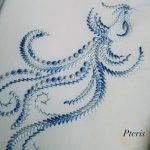 Bird with a flying feather machine embroidery design showing a gracefully stitched stylized bird trailing an elegant, flowing ornamental line-work feather motif, displayed flat on light blue fabric.