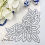 Richelieu cutwork machine embroidery design showcasing an elegant grey-blue floral corner pattern stitched onto a white fabric napkin, styled flat with white blossoms and blue beads.