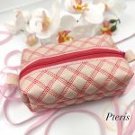 ITH quilted makeup bag machine embroidery design showing a completed cream faux leather cosmetic pouch with an elegant quilted texture, a matching zipper closure, and a professionally lined interior, styled flat on a plain background.