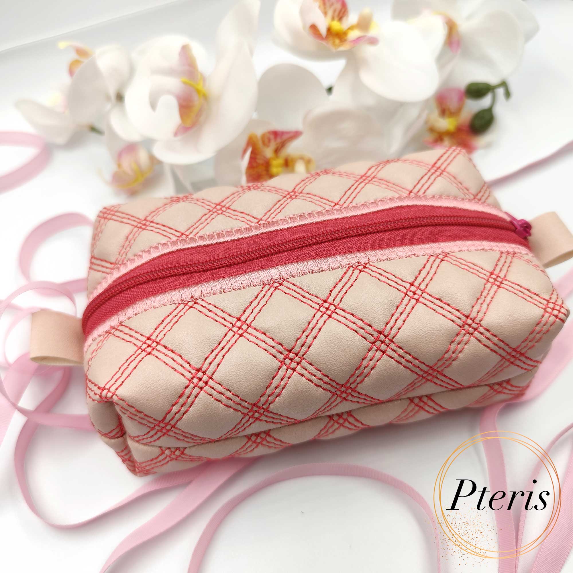 ITH quilted makeup bag machine embroidery design showing a completed cream faux leather cosmetic pouch with an elegant quilted texture, a matching zipper closure, and a professionally lined interior, styled flat on a plain background.