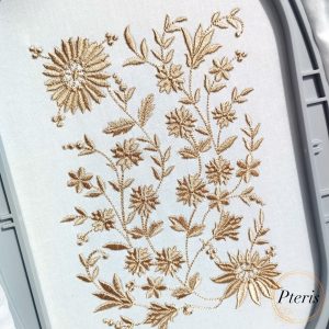 An elegant, monochrome botanical machine embroidery design featuring delicate daisies and meadow grasses stitched with a golden-beige thread on white fabric within a grey hoop, as shown in Daisy-and-Meadow-Grasses-Infinity-Border-Machine-Embroidery-Design-