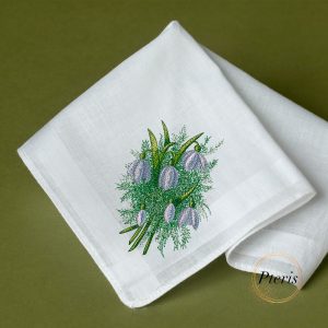 A delicate machine embroidery design of a spring flower bouquet with soft purple snowdrop blossoms and detailed green foliage, beautifully stitched on the corner of a folded white linen handkerchief, resting on a dark green surface, as shown in Easter-embroidery-design7.jpg.