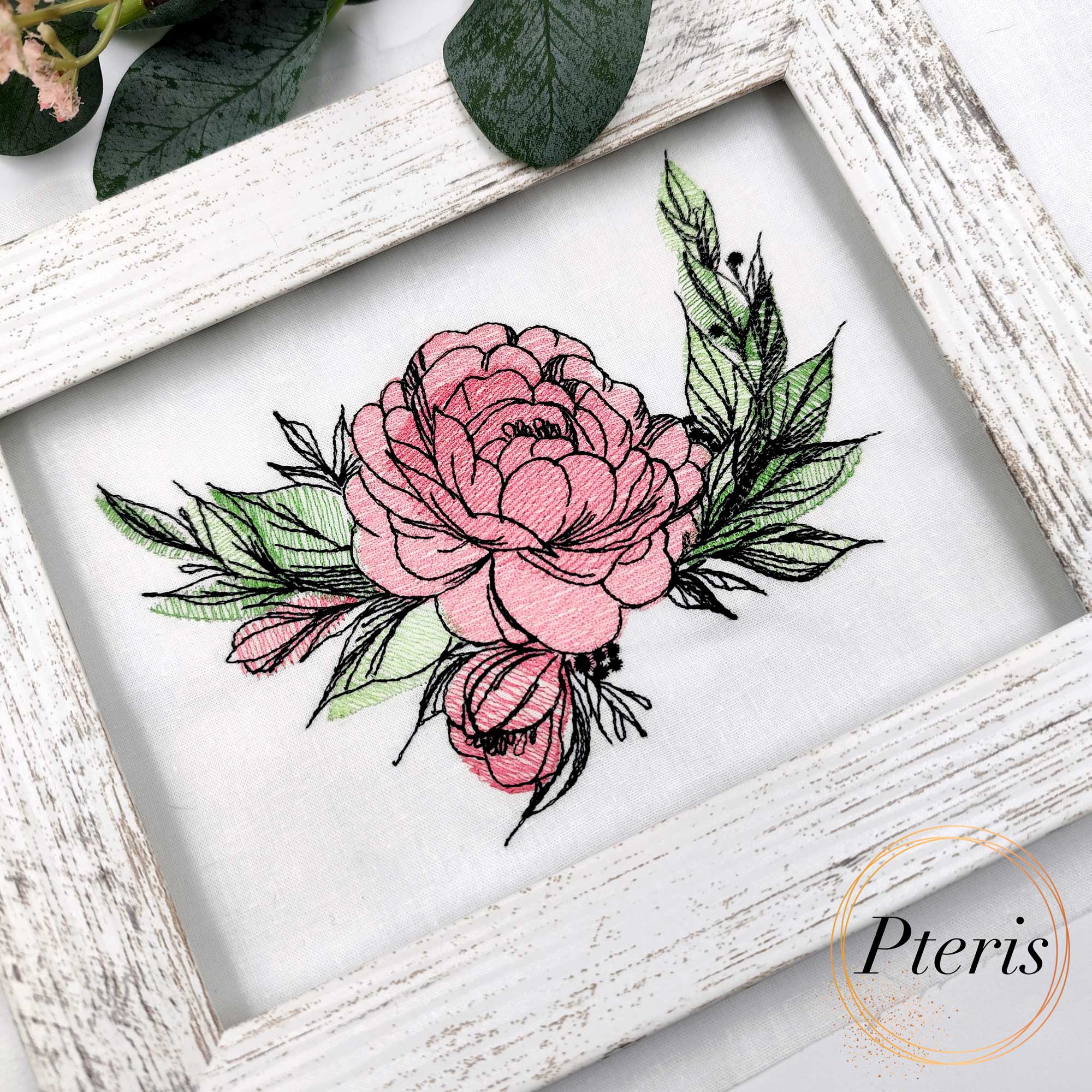 A beautiful sketch-style machine embroidery design of a pink peony flower with detailed black outlines and green leaves, stitched on white fabric and showcased in a rustic white wooden frame, as shown in Peony Embroidery Design