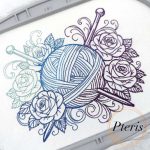 Machine embroidery design featuring a detailed ball of yarn with two knitting needles, surrounded by elegant roses and decorative swirls, stitched on white fabric using a blue-to-purple gradient thread.