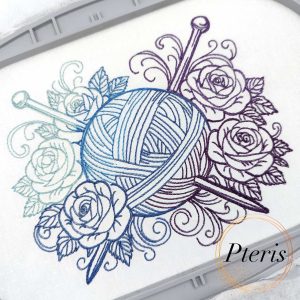 Machine embroidery design featuring a detailed ball of yarn with two knitting needles, surrounded by elegant roses and decorative swirls, stitched on white fabric using a blue-to-purple gradient thread.