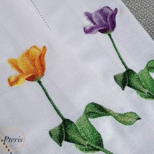 Close-up of machine-embroidered tulips in orange-yellow and purple colors with detailed shaded green leaves on a white linen towel.